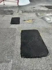 Two black rectangular patches on a weathered gray concrete surface.