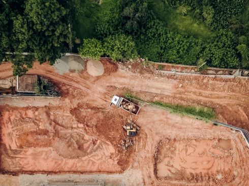 Aerial view of a muddy construction site with excavators and a white truck near a forest edge