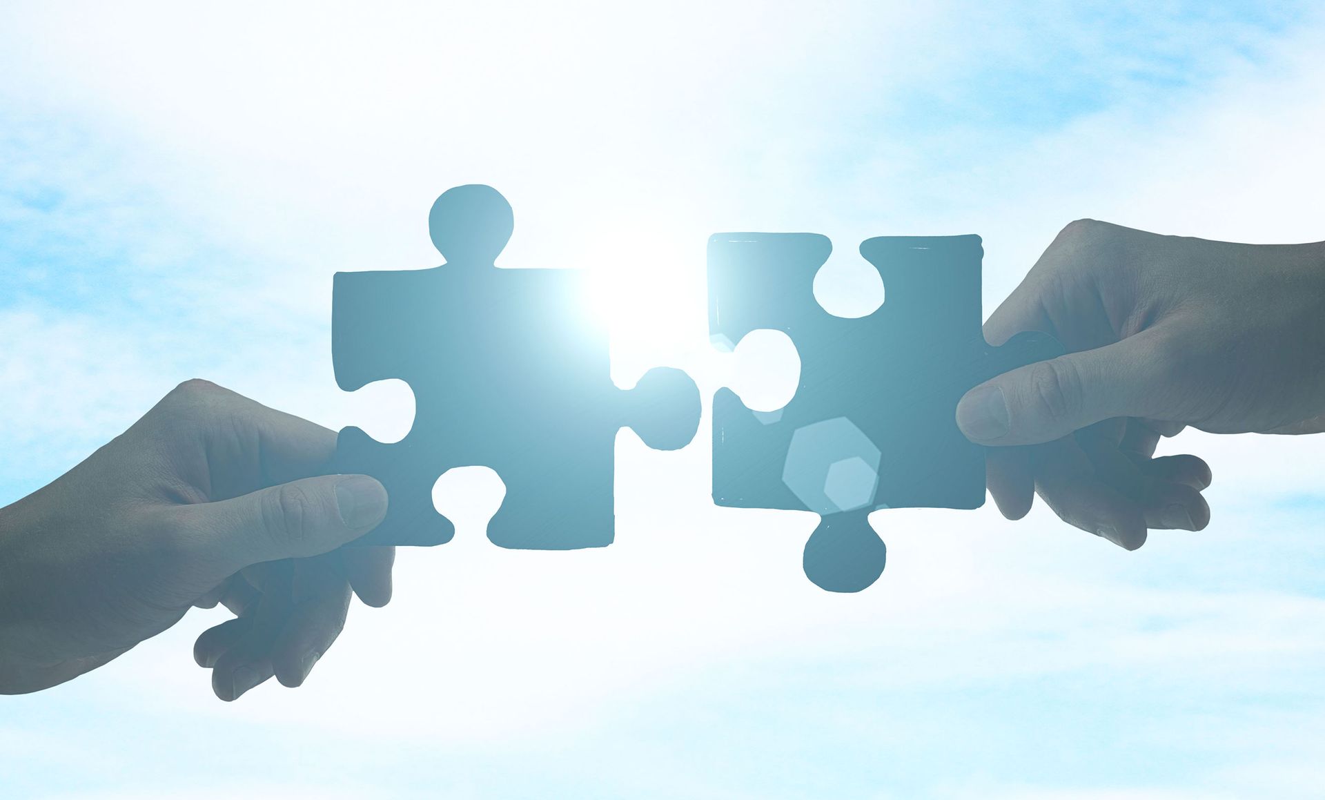 Two people are holding puzzle pieces in their hands against a blue sky.