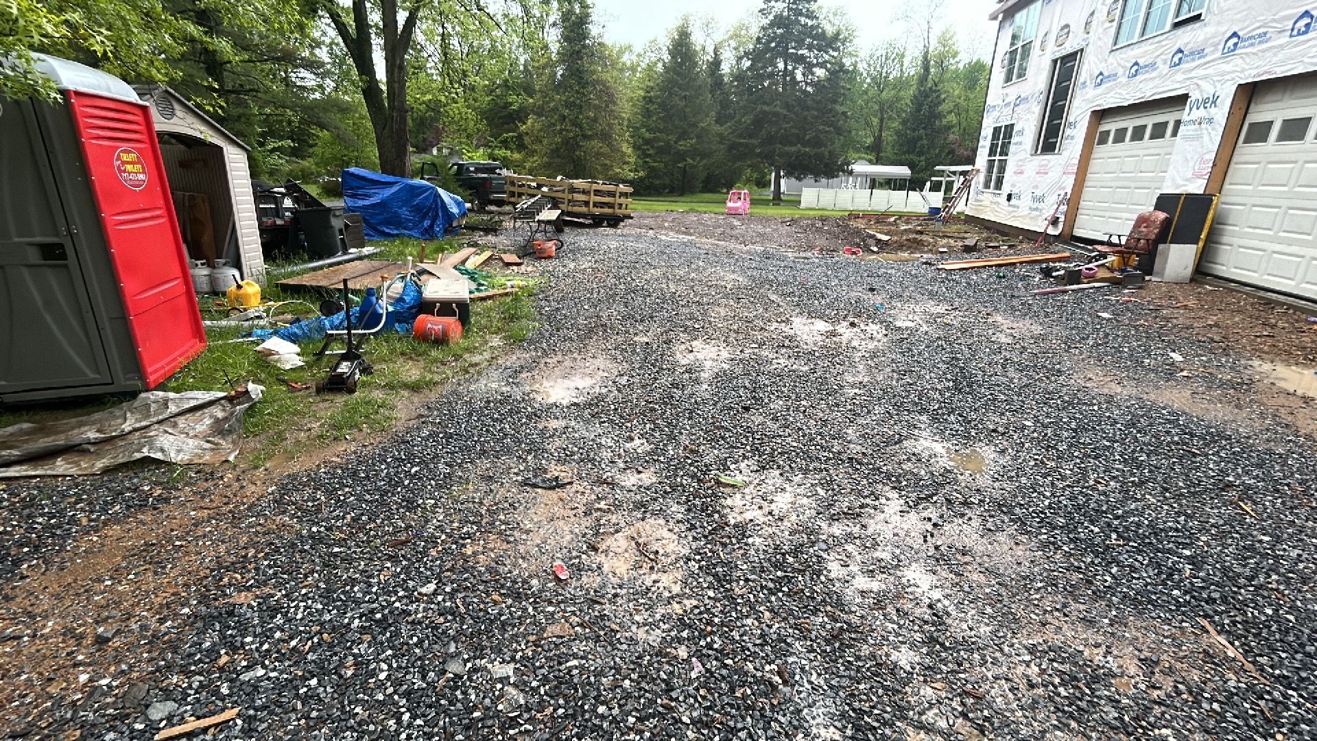 Construction site driveway: gravel, porta-potty, unfinished house with garage.