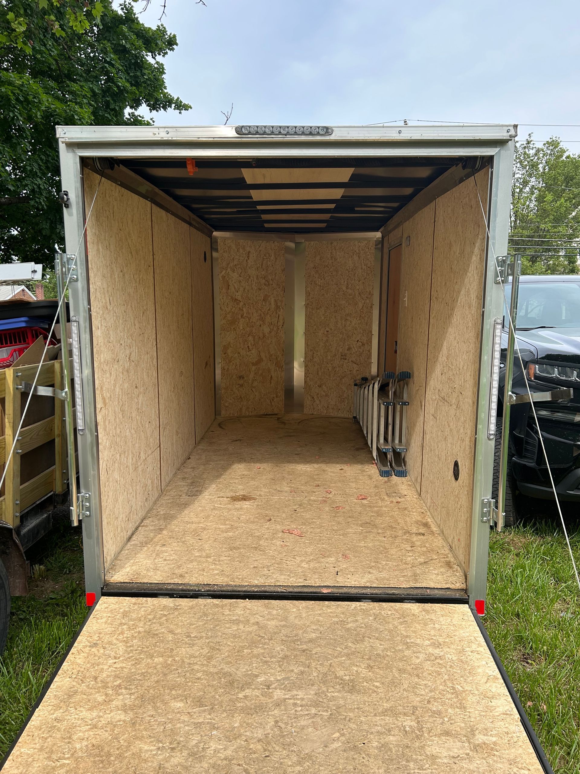 Open empty cargo trailer, wood interior, ramp down, parked on grass.