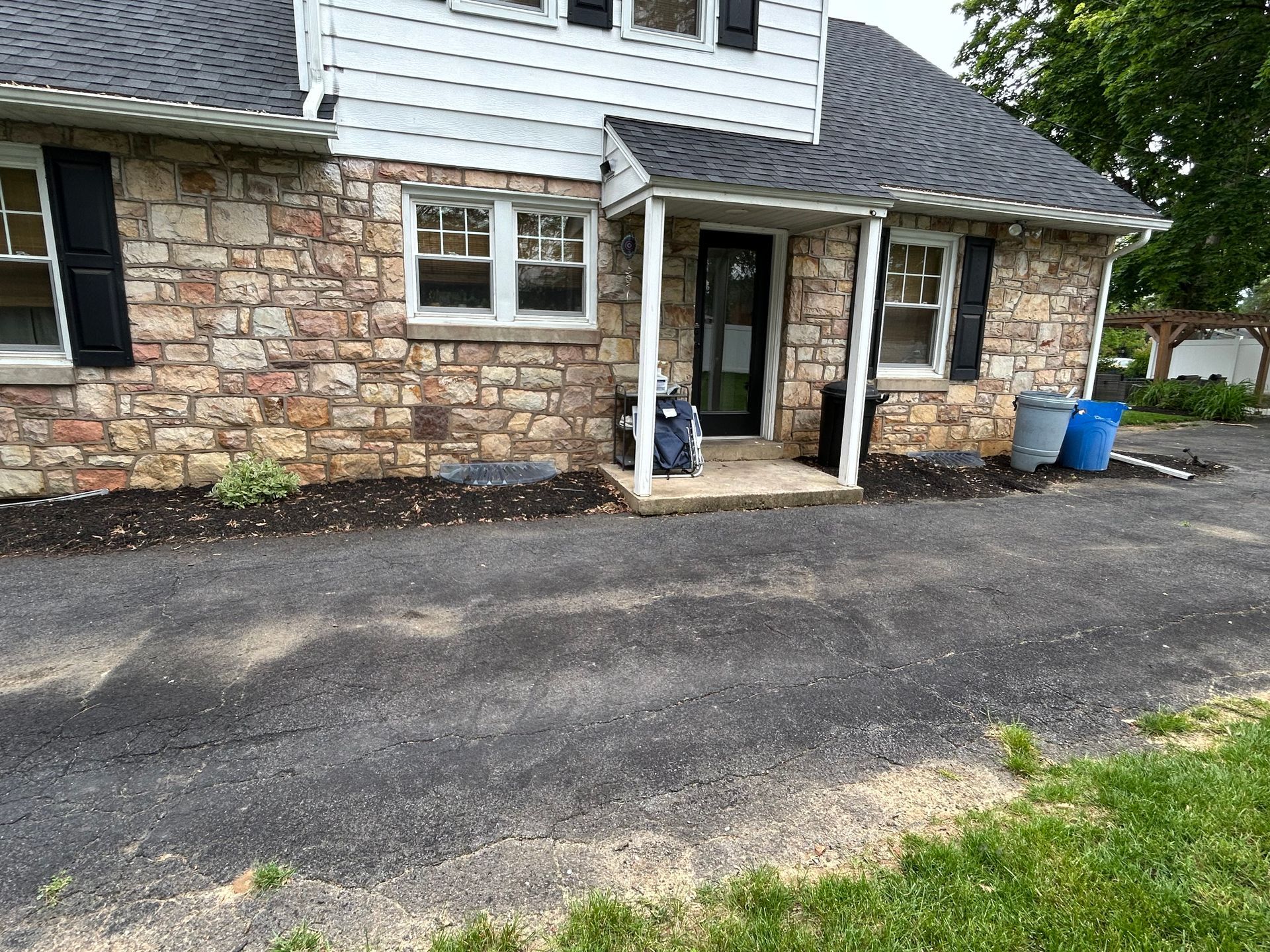 Stone house with black shutters, front porch, and asphalt driveway.