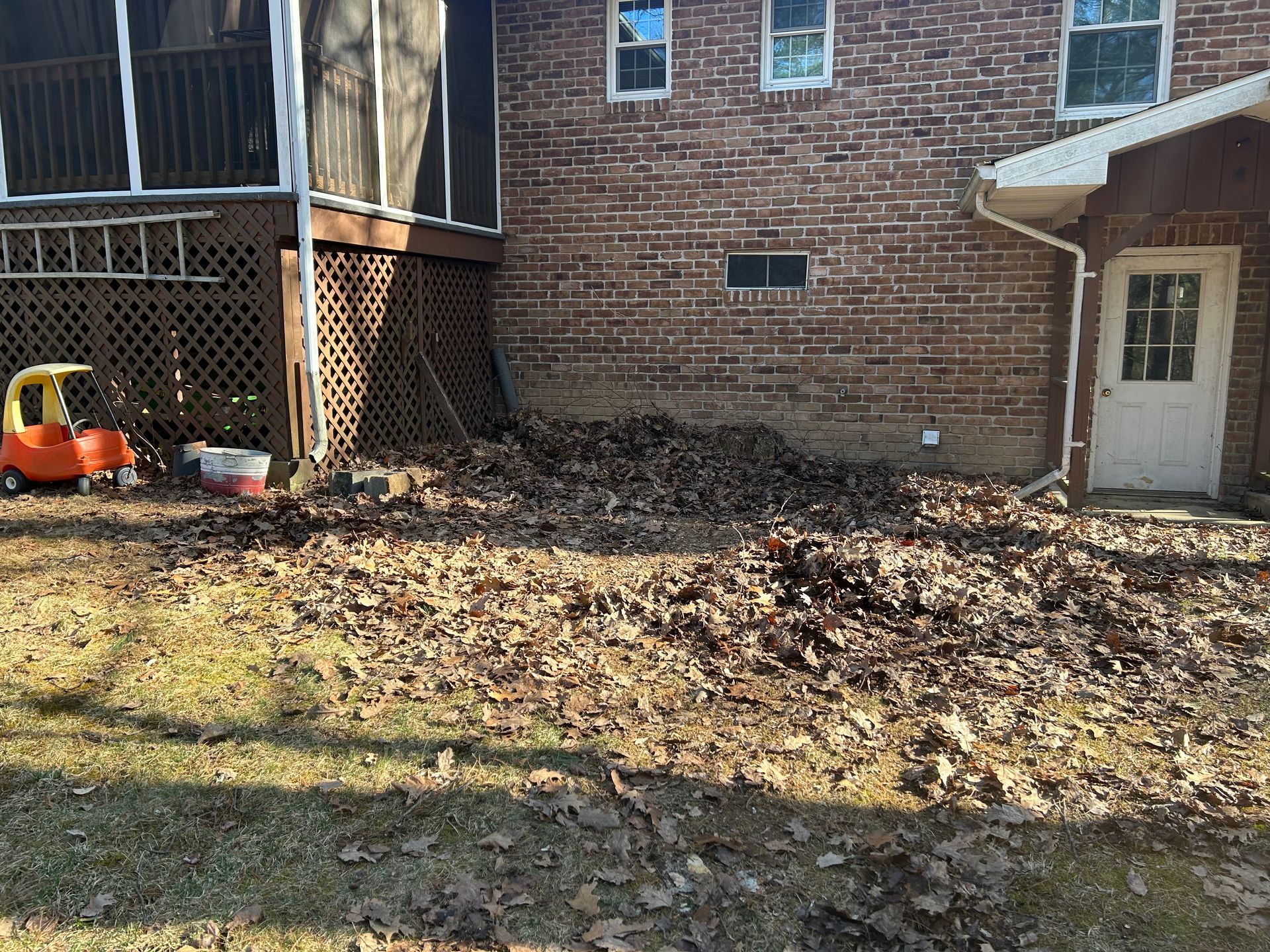 A yard covered in fallen leaves near a brick house and a deck.