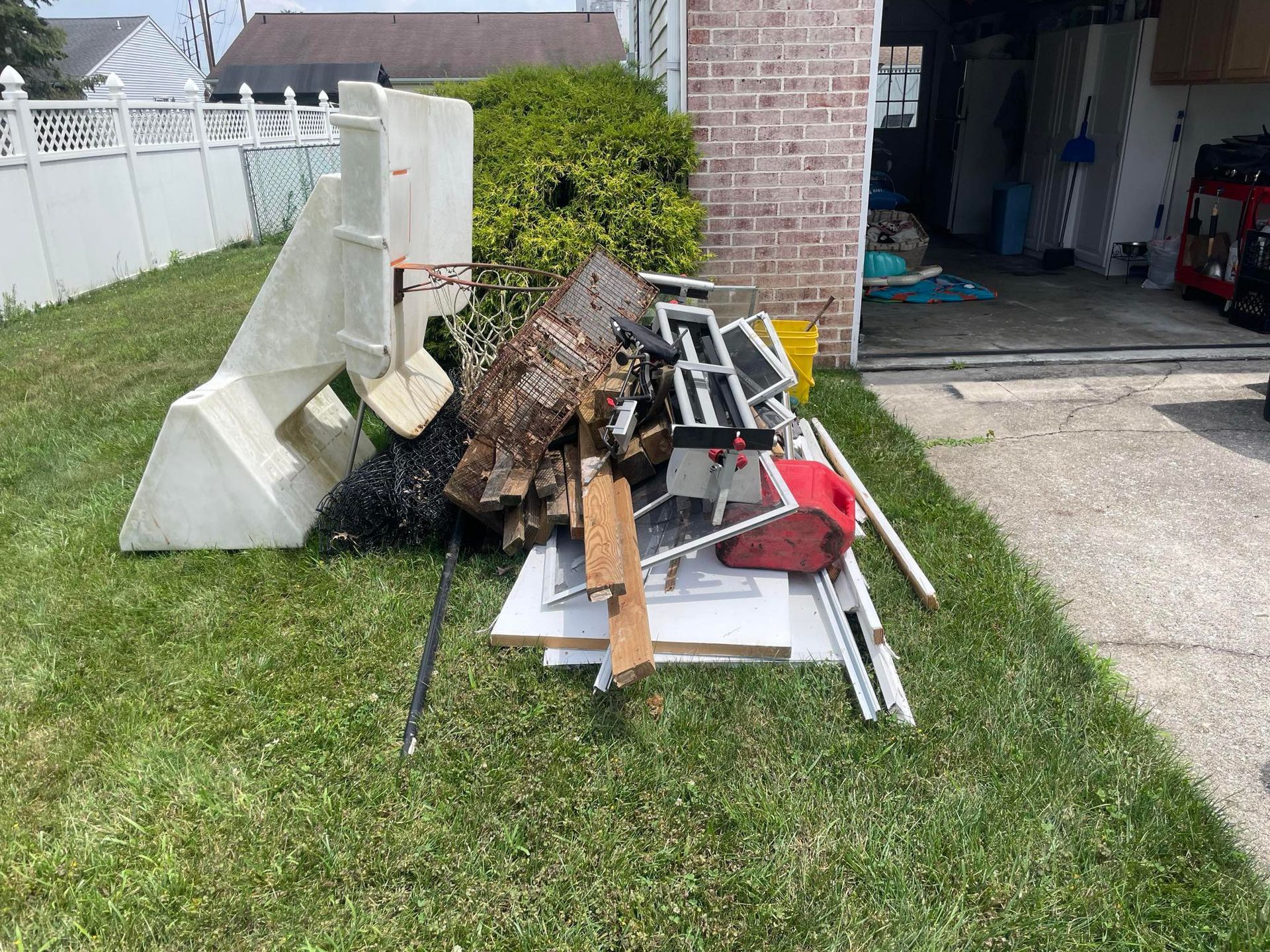 Pile of debris, including white plastic forms, scrap wood, and metal, on a lawn next to a brick building.
