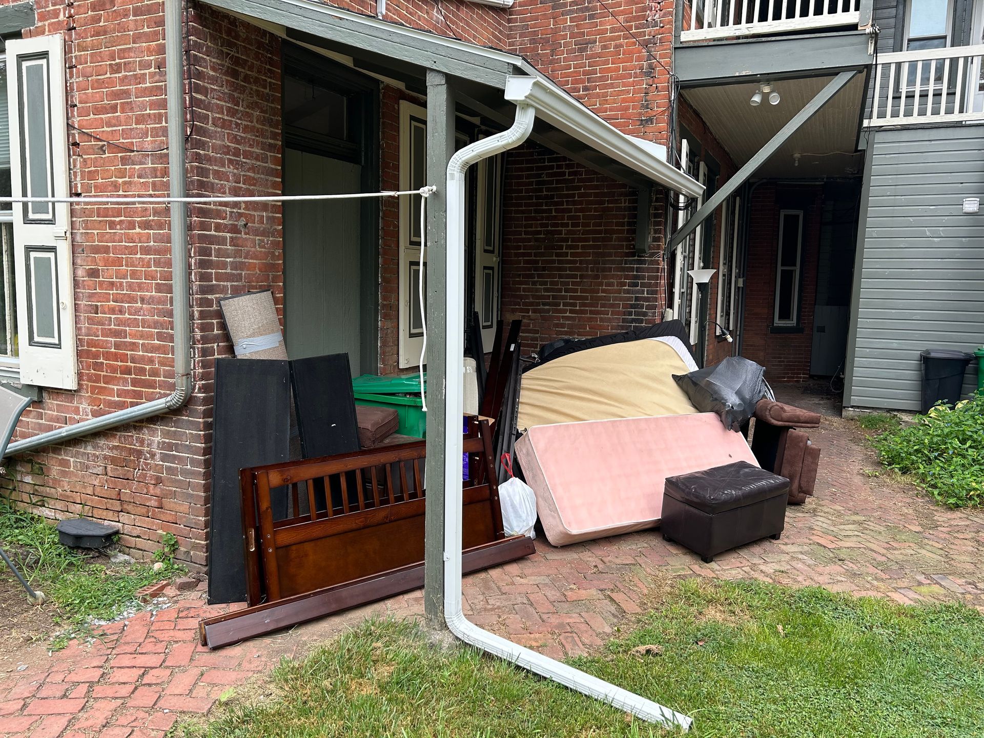 Pile of discarded furniture outside a brick building. Includes mattress, headboard, and other items.