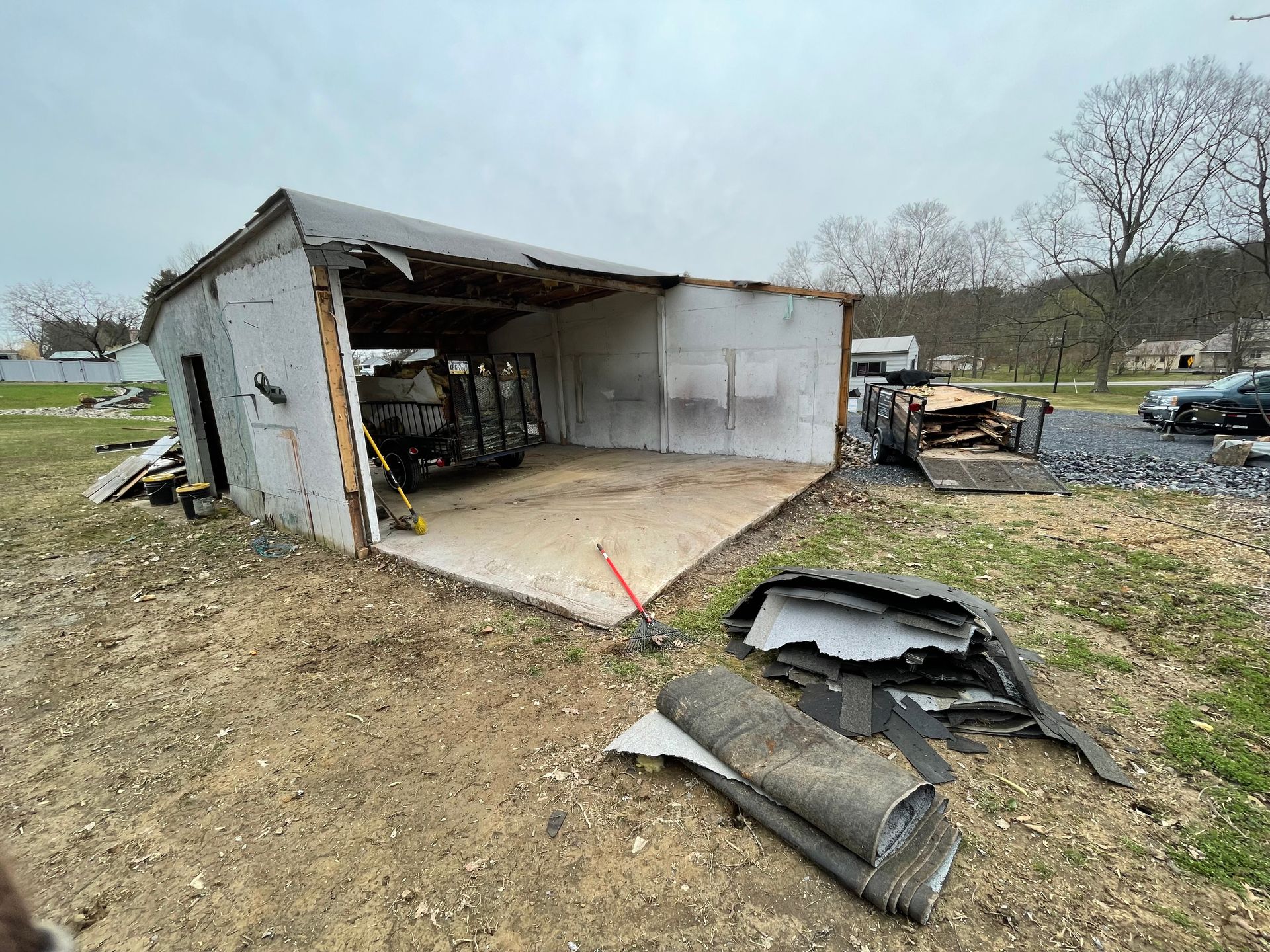 Damaged shed with collapsed roof and debris on the ground; outdoors.