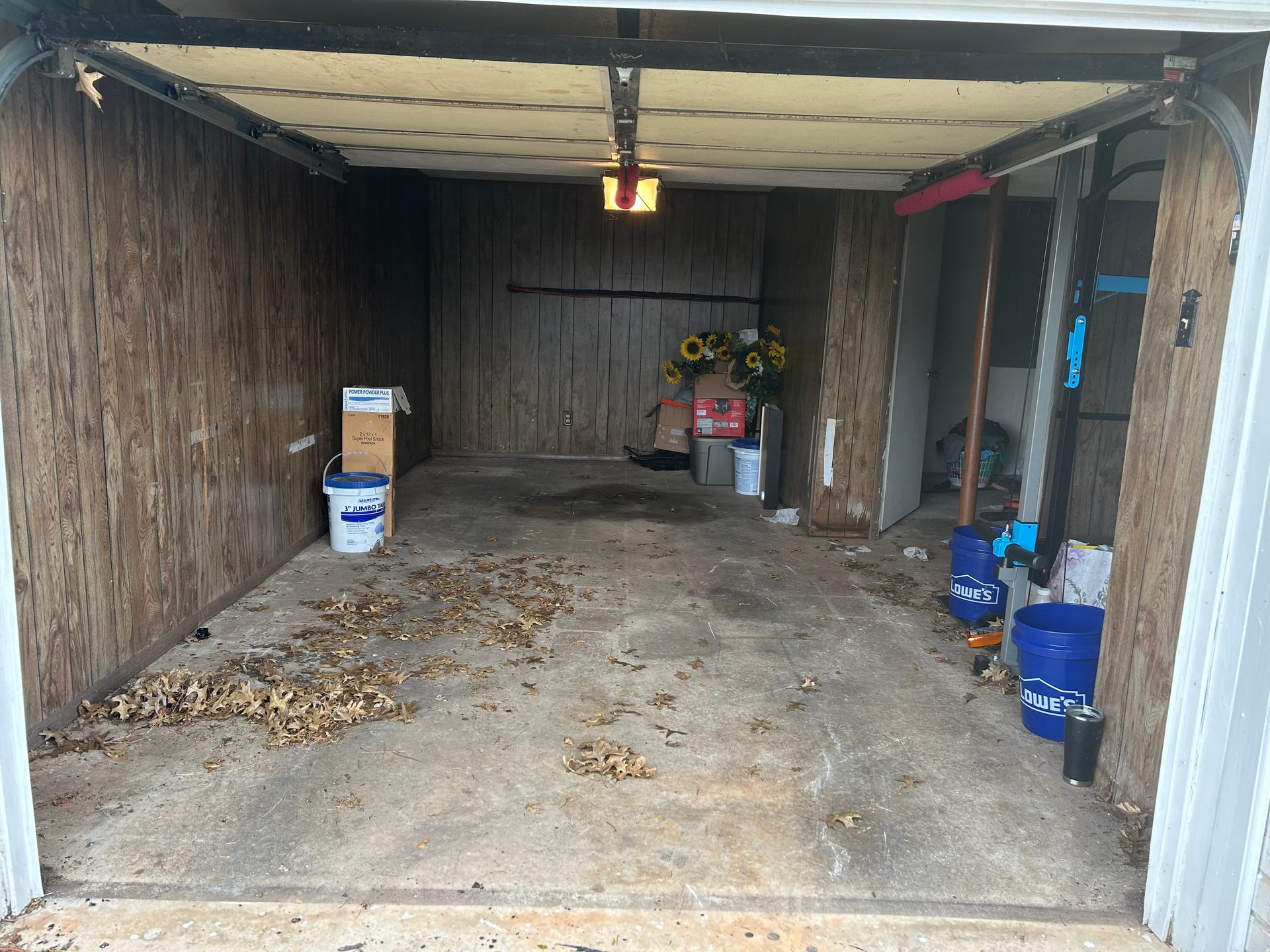 Empty garage with debris on the floor and items stored along the walls.