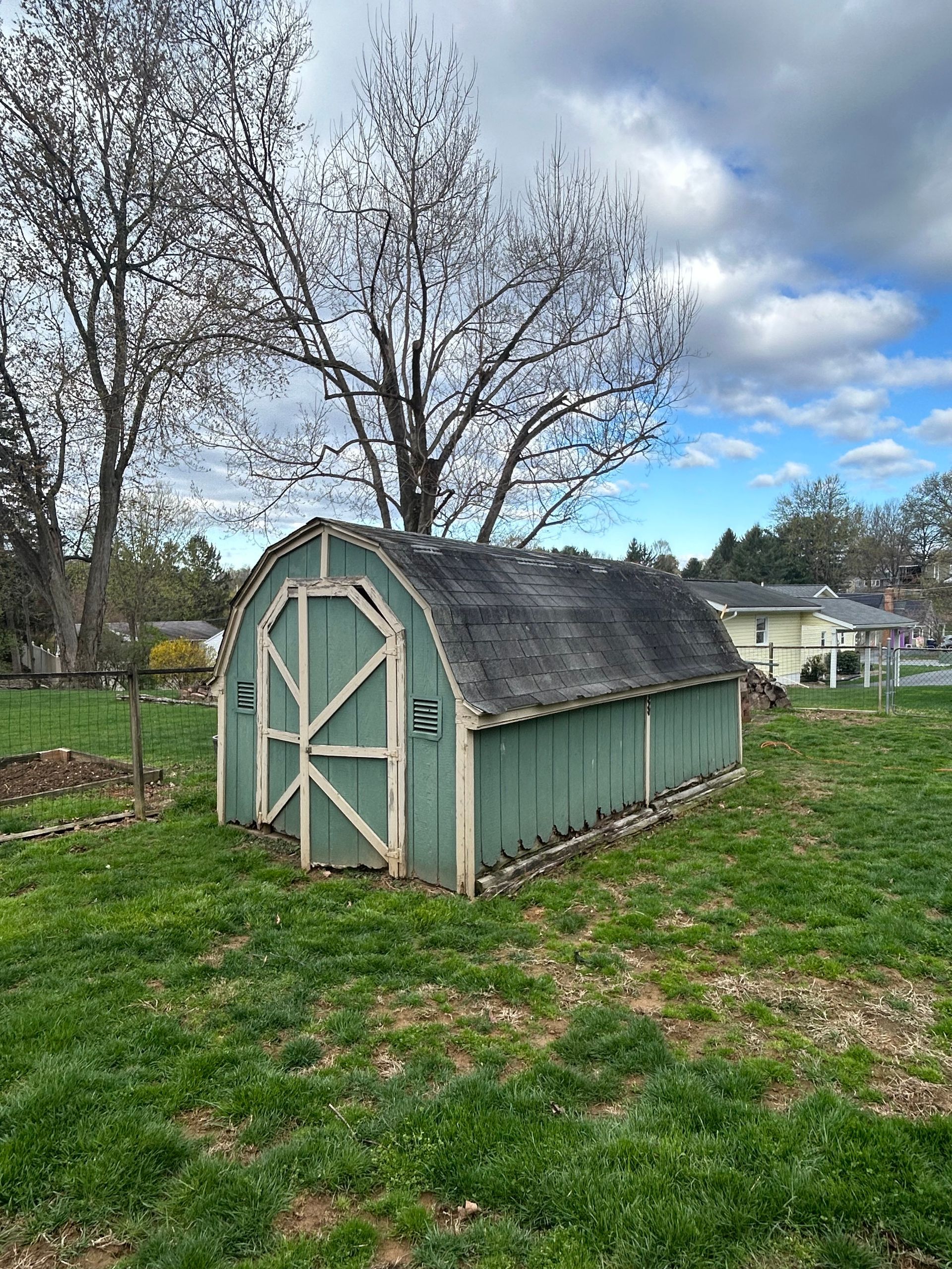 Green shed with arched roof on a grassy lawn, under a cloudy sky, with trees in the background.