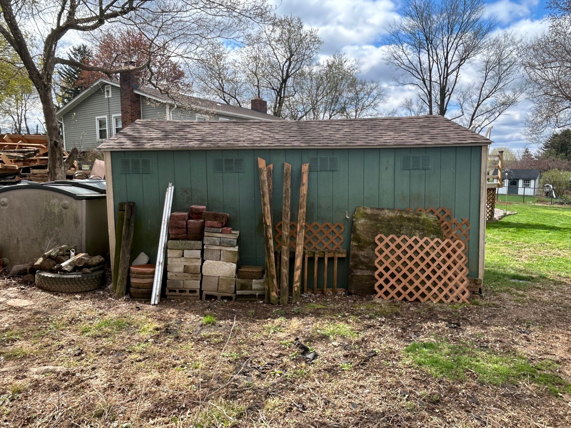 Green shed with various building materials like bricks and latticework in a grassy backyard.