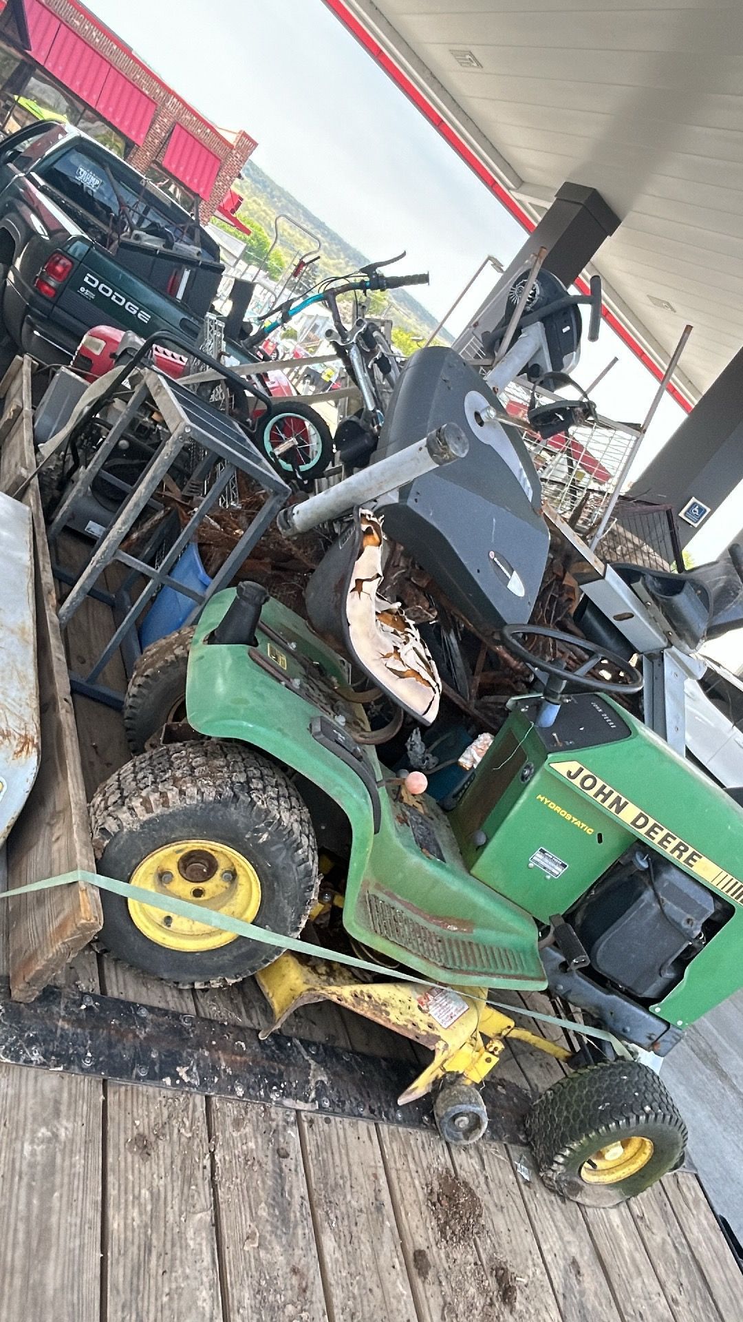 A green John Deere riding lawnmower is loaded on a trailer with scrap metal.