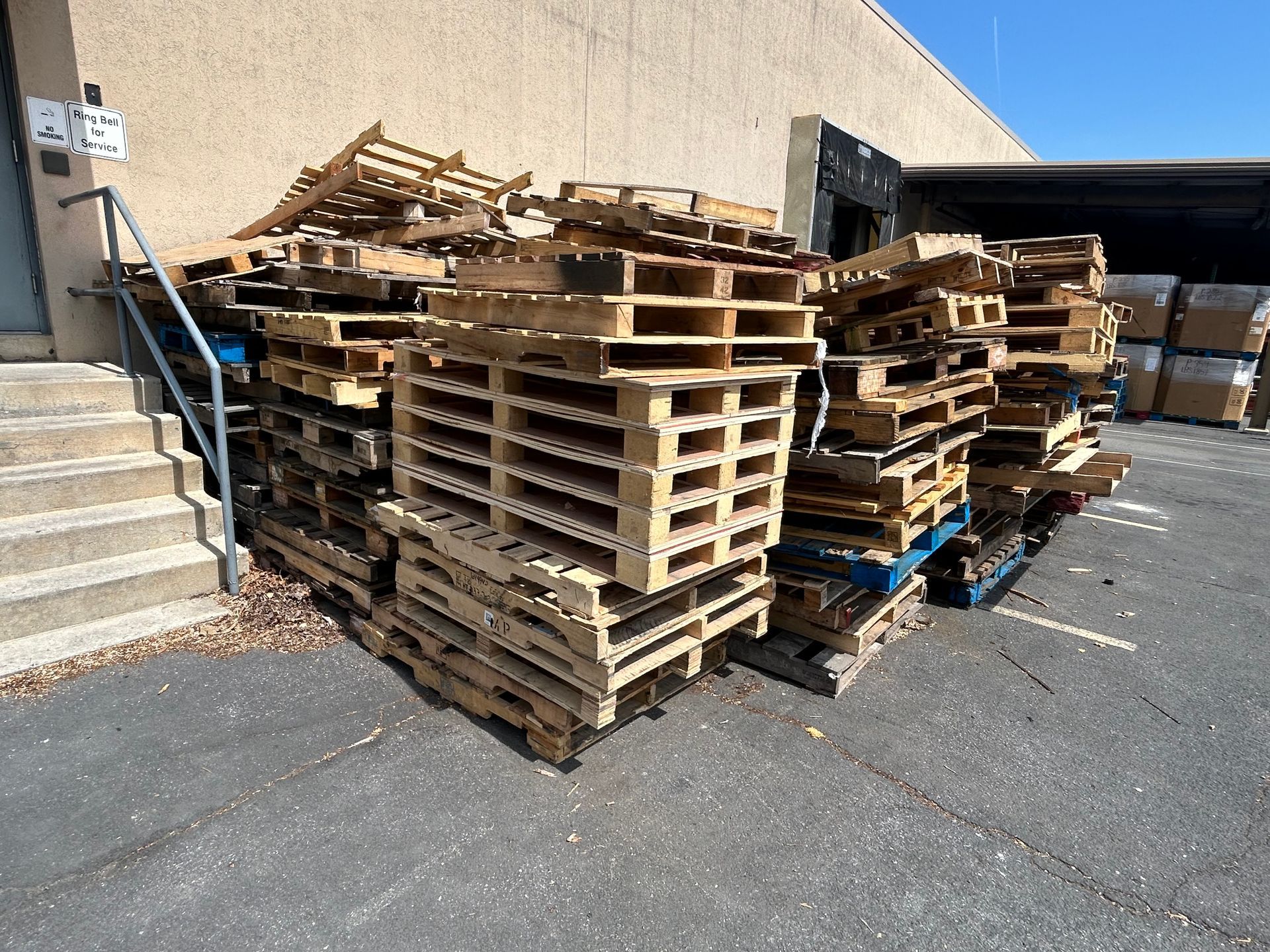 Pile of wooden pallets stacked outside a building on an asphalt surface.