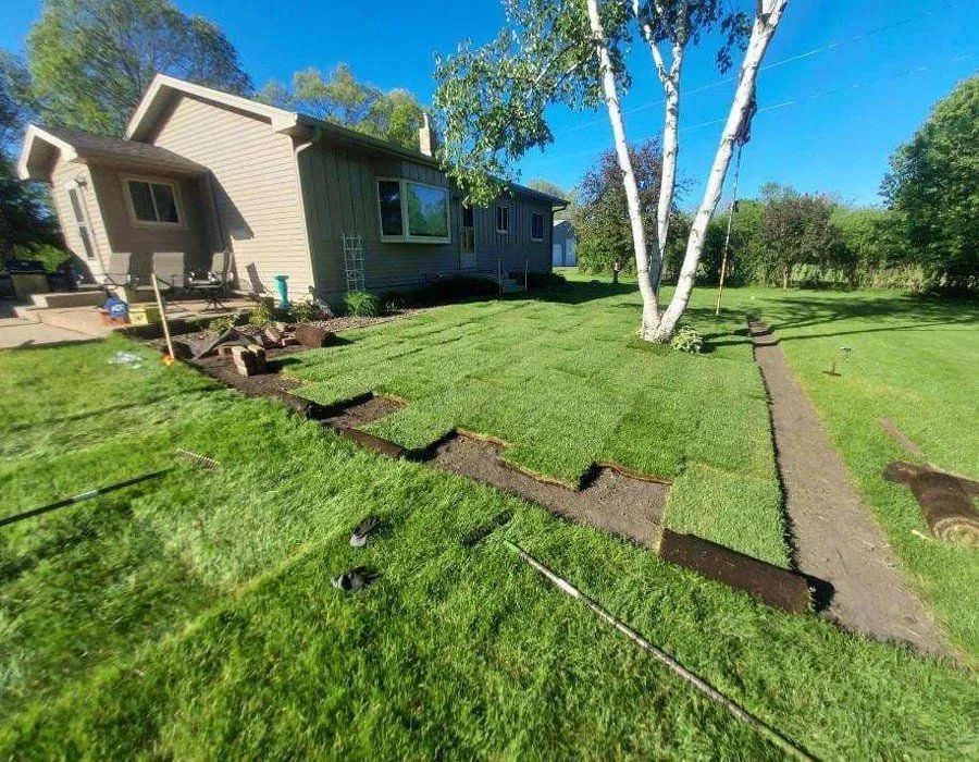 A house with a yard undergoing a landscaping project, featuring freshly laid patches of green sod on dirt ground.