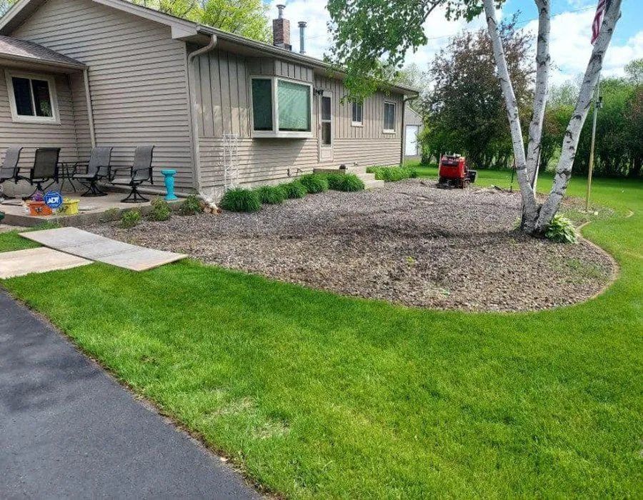 A tan house with a gravel garden bed, a paved walkway, and a green lawn on a sunny day.