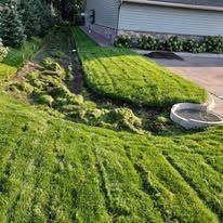 Freshly mowed lawn with a strip of tall grass along a hillside near a house and concrete drainage structure.