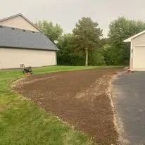 A freshly mulched garden bed curves along a paved driveway between two houses in a residential yard.