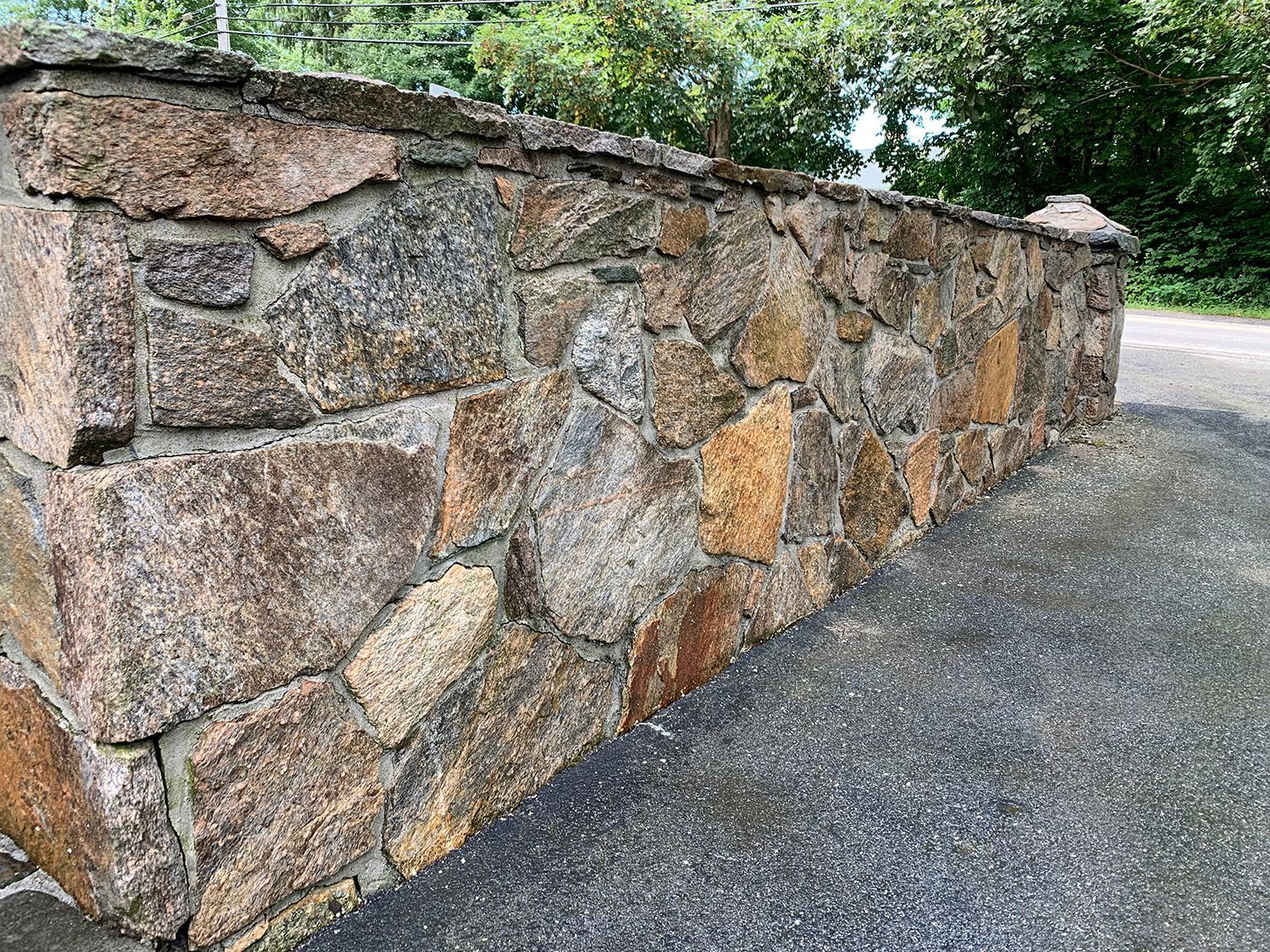 A large stone wall is sitting on the side of a road.