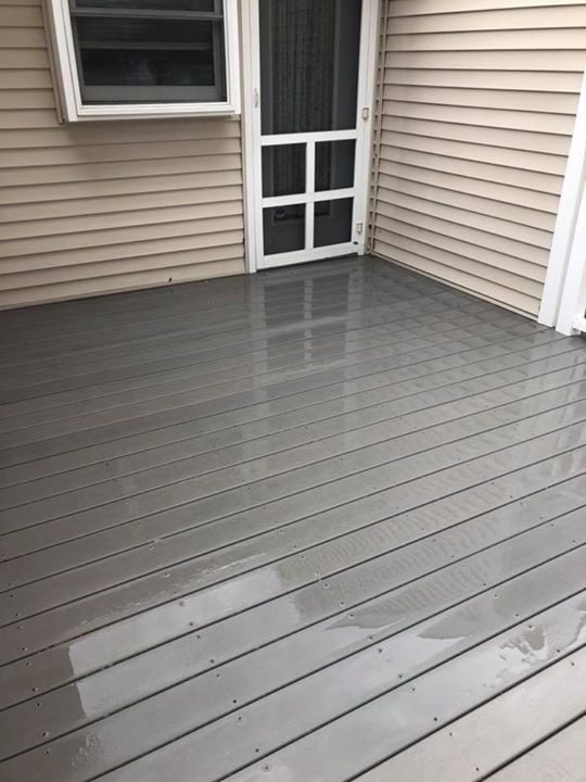 A gray deck next to a house with a screen door.