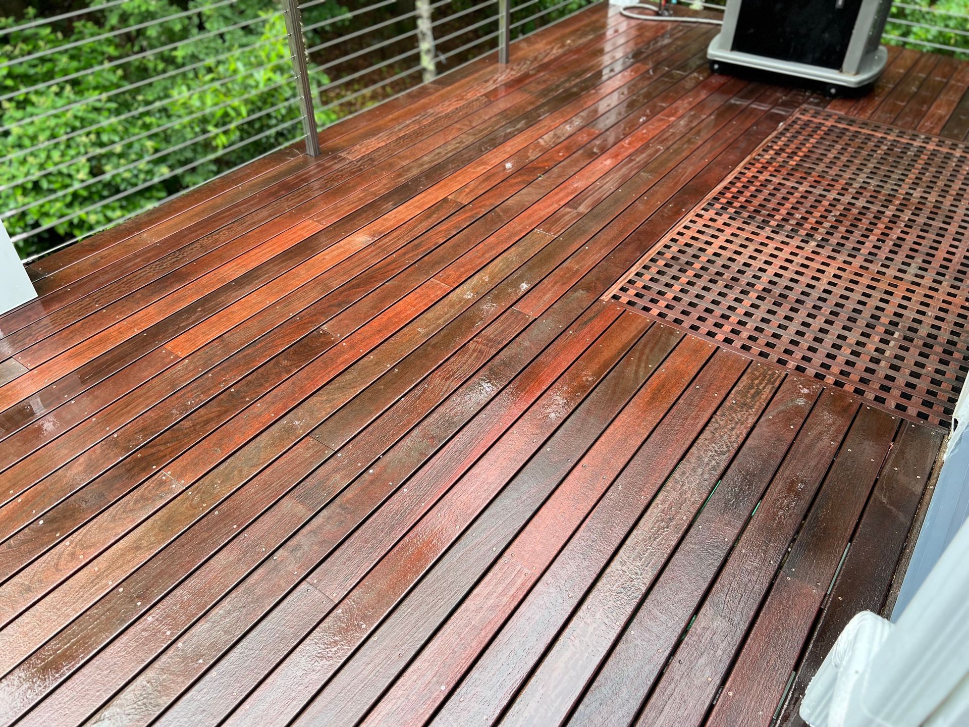 A wooden deck with a stainless steel railing and a grill on it.