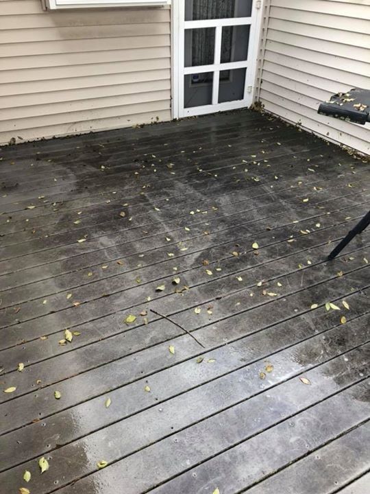 A dirty wooden deck with leaves on it in front of a house.