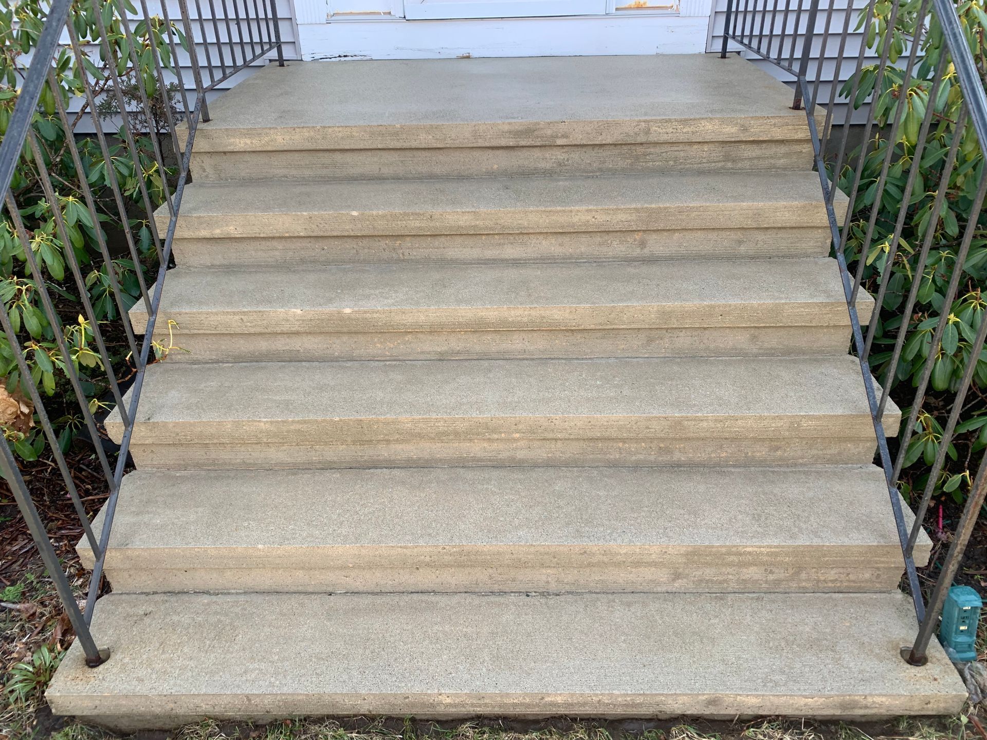 A set of concrete stairs leading up to a house with a metal railing.