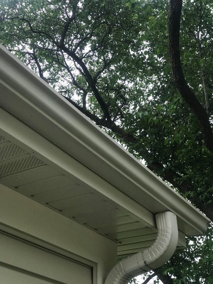 A white gutter on the side of a house with trees in the background.