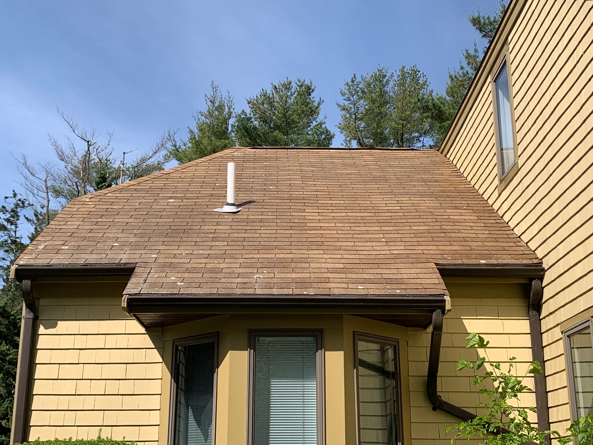 A yellow house with a brown roof and a white chimney.