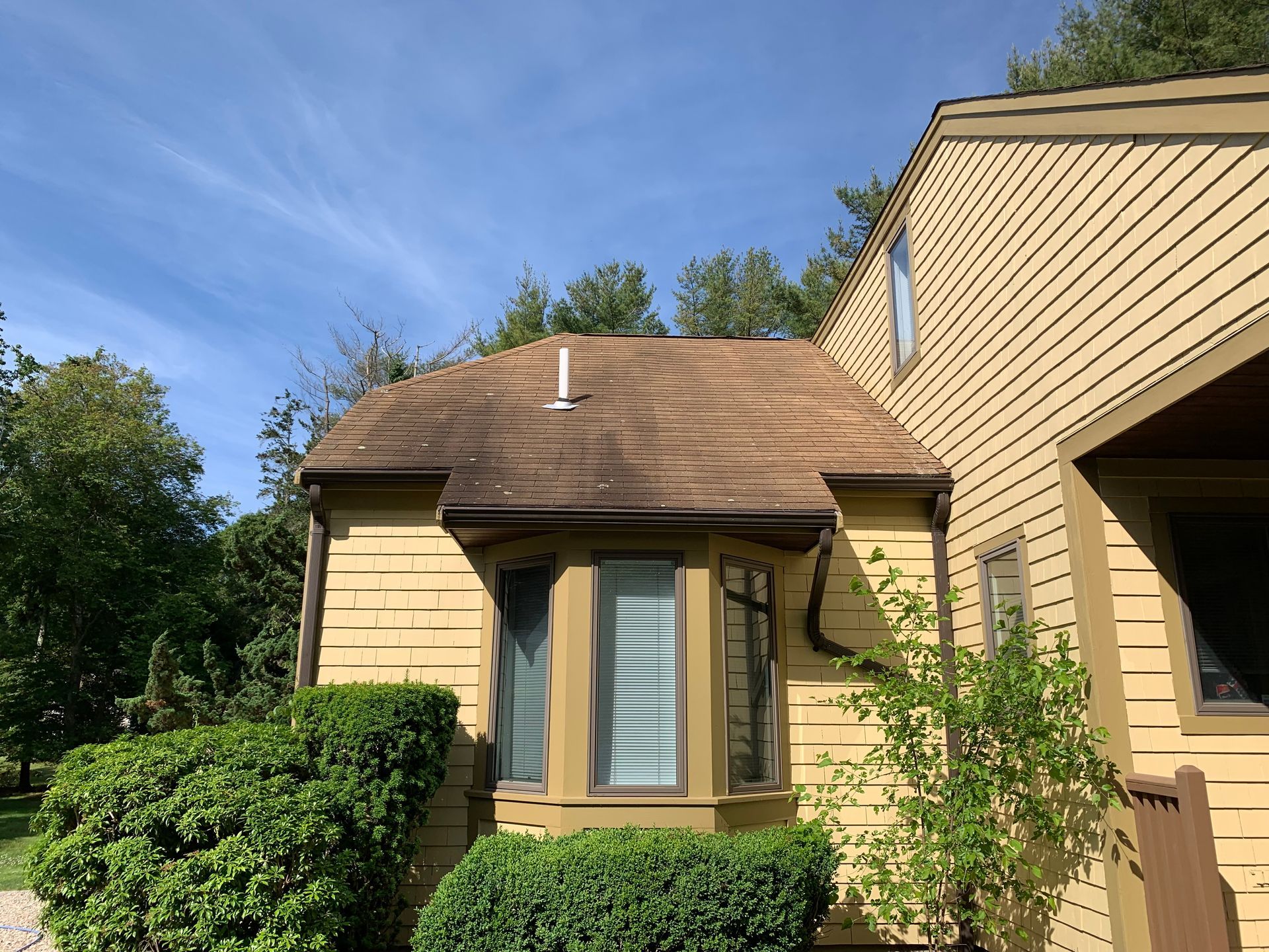 A yellow house with a brown roof and a bay window.