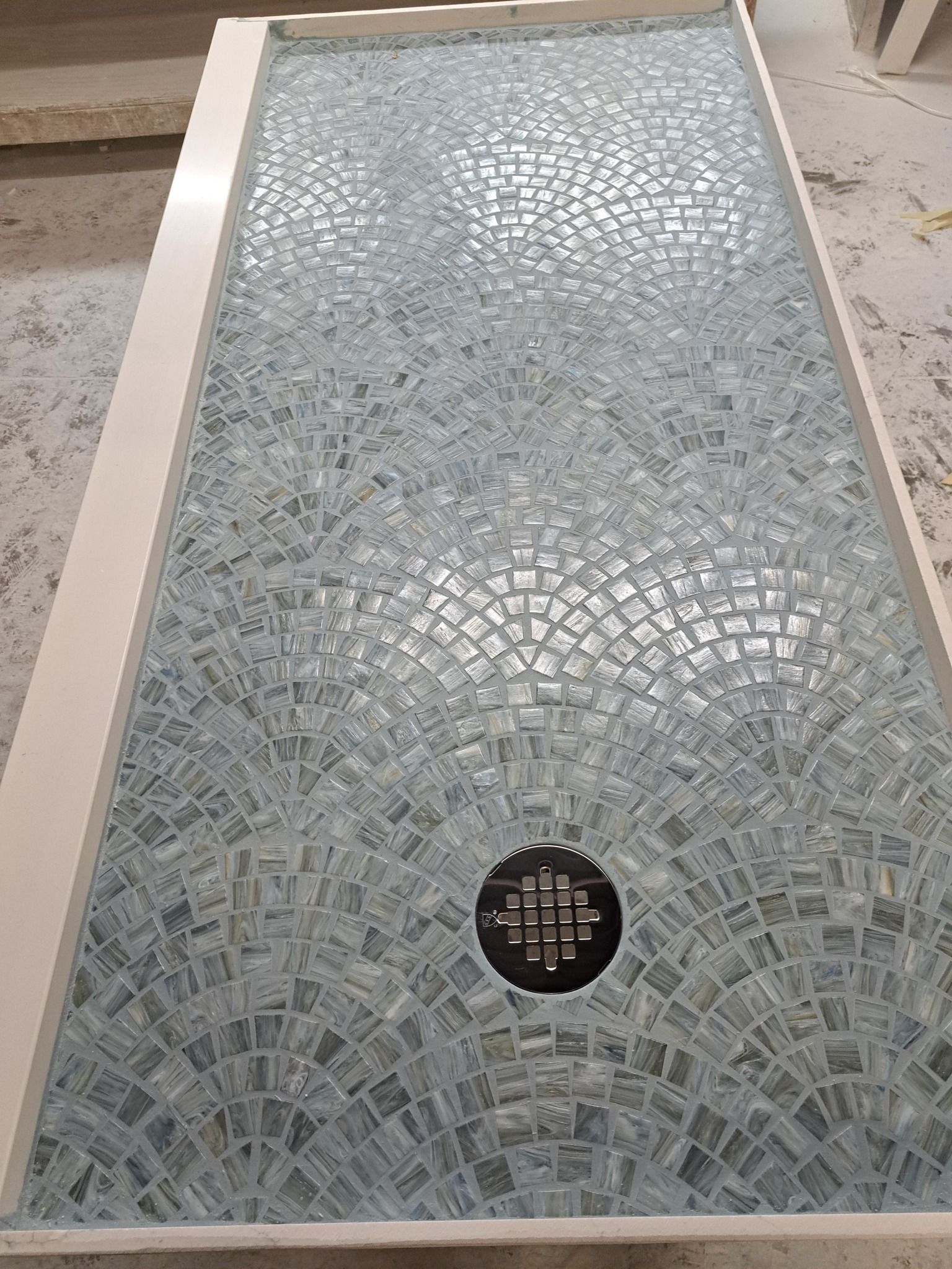 A shower stall with a mosaic tile floor and a drain.