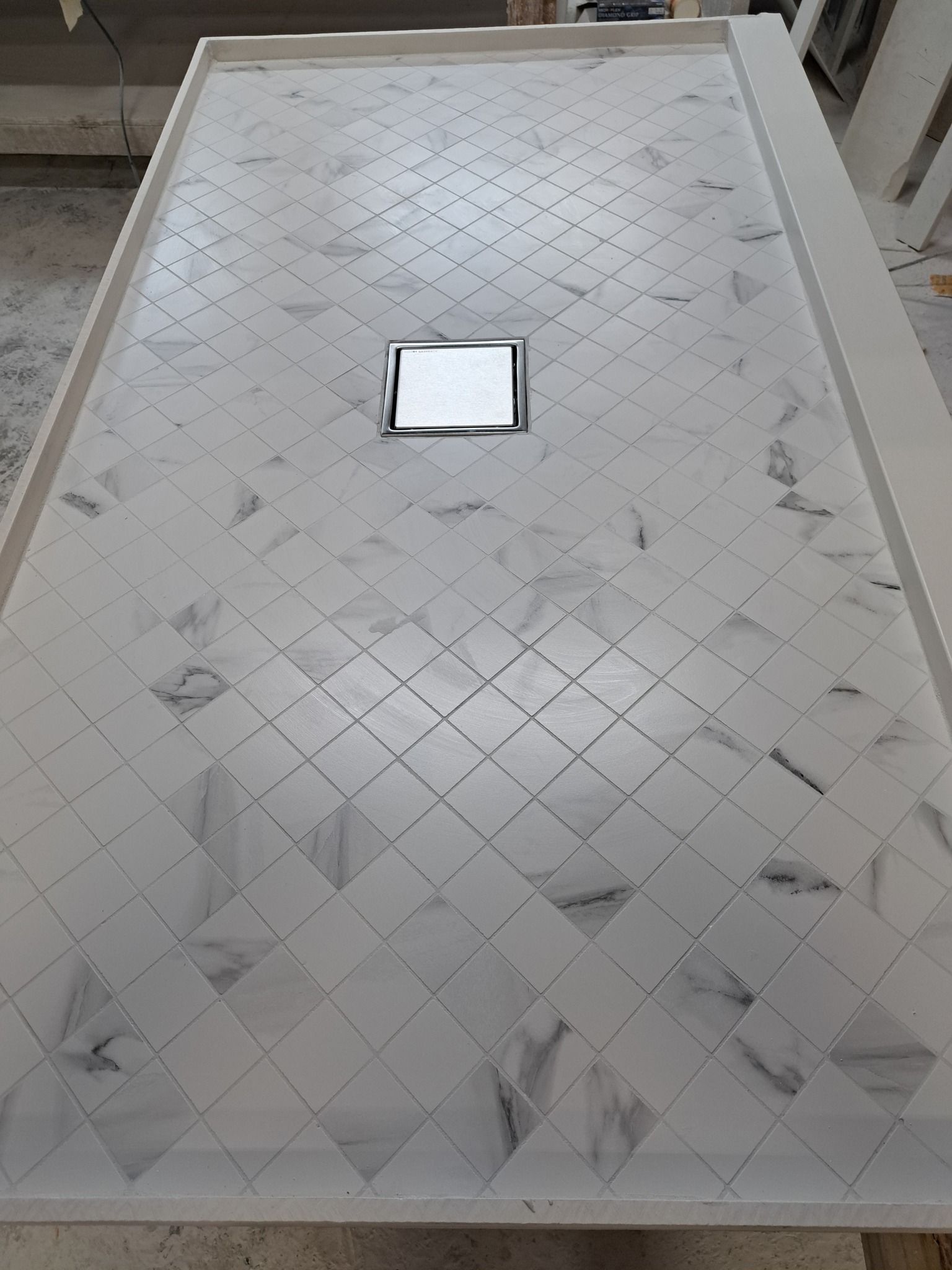 A white marble shower tray with a drain on the floor.