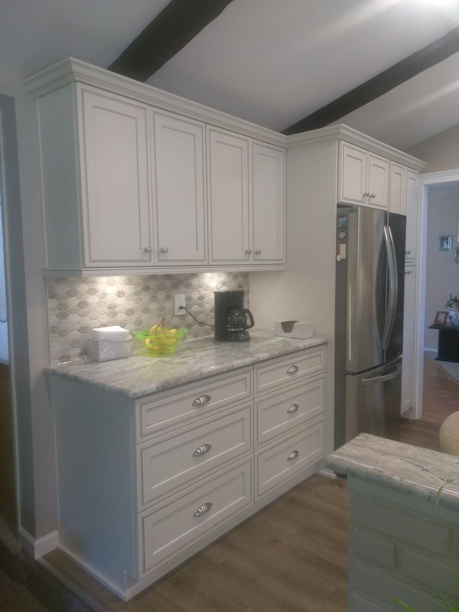 A kitchen with white cabinets , stainless steel appliances , a coffee maker , and a refrigerator.
