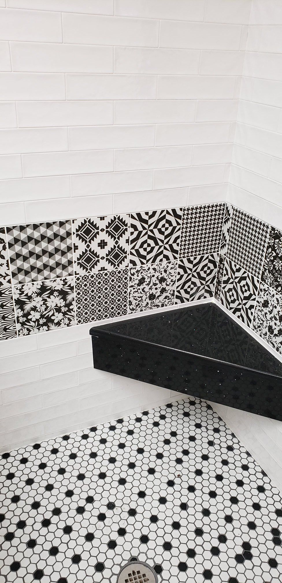 A bathroom with black and white tiles and a black corner shelf.