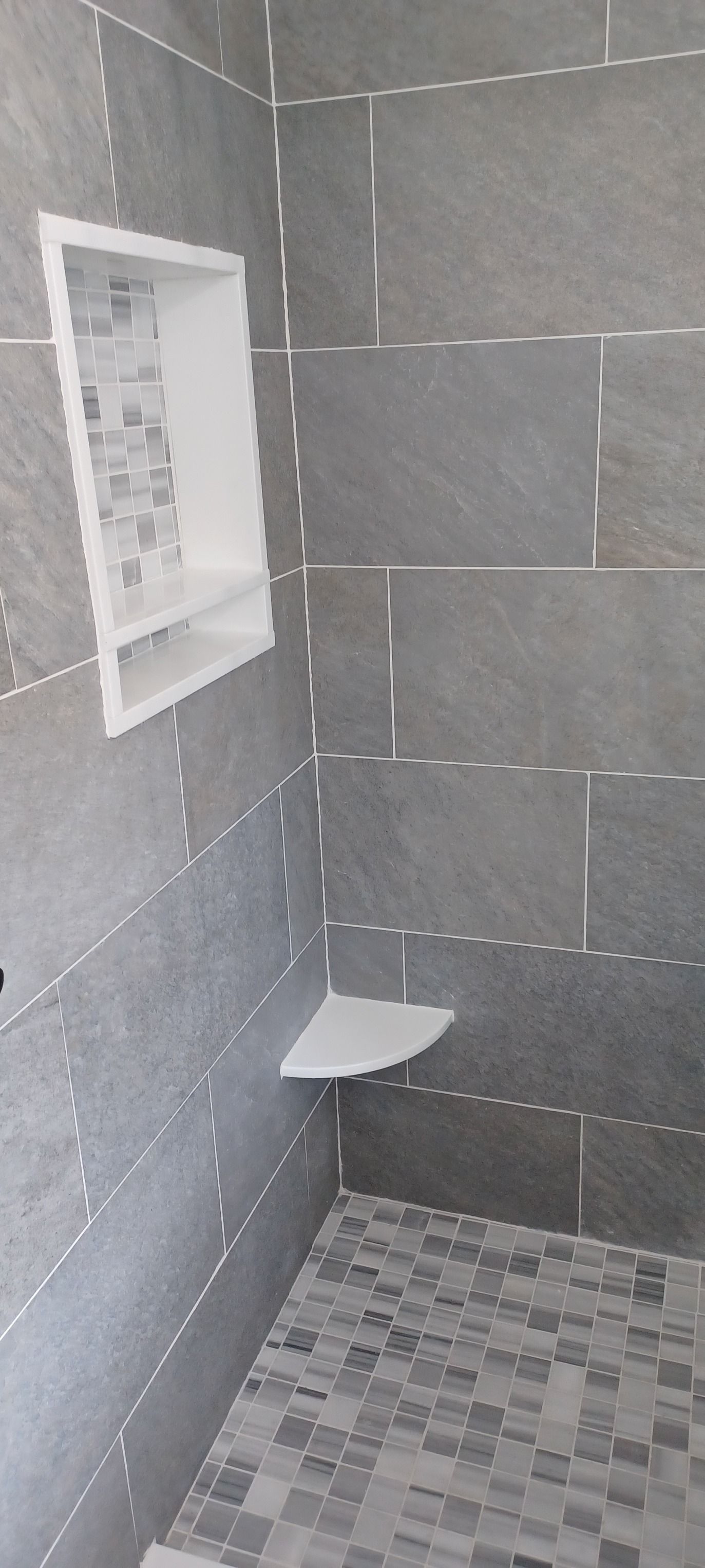 A black and white photo of a shower with a corner shelf.