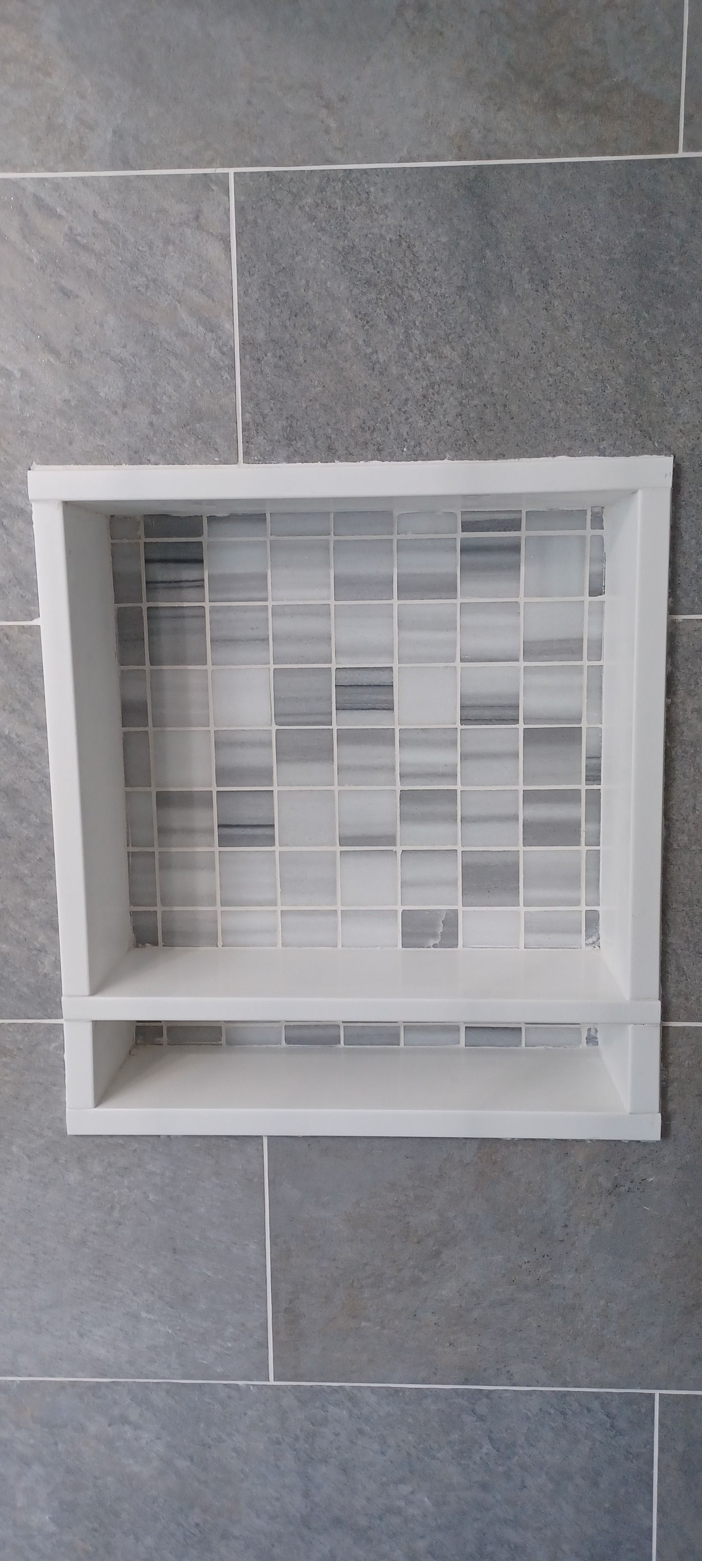 A white shelf is sitting on top of a tiled wall.