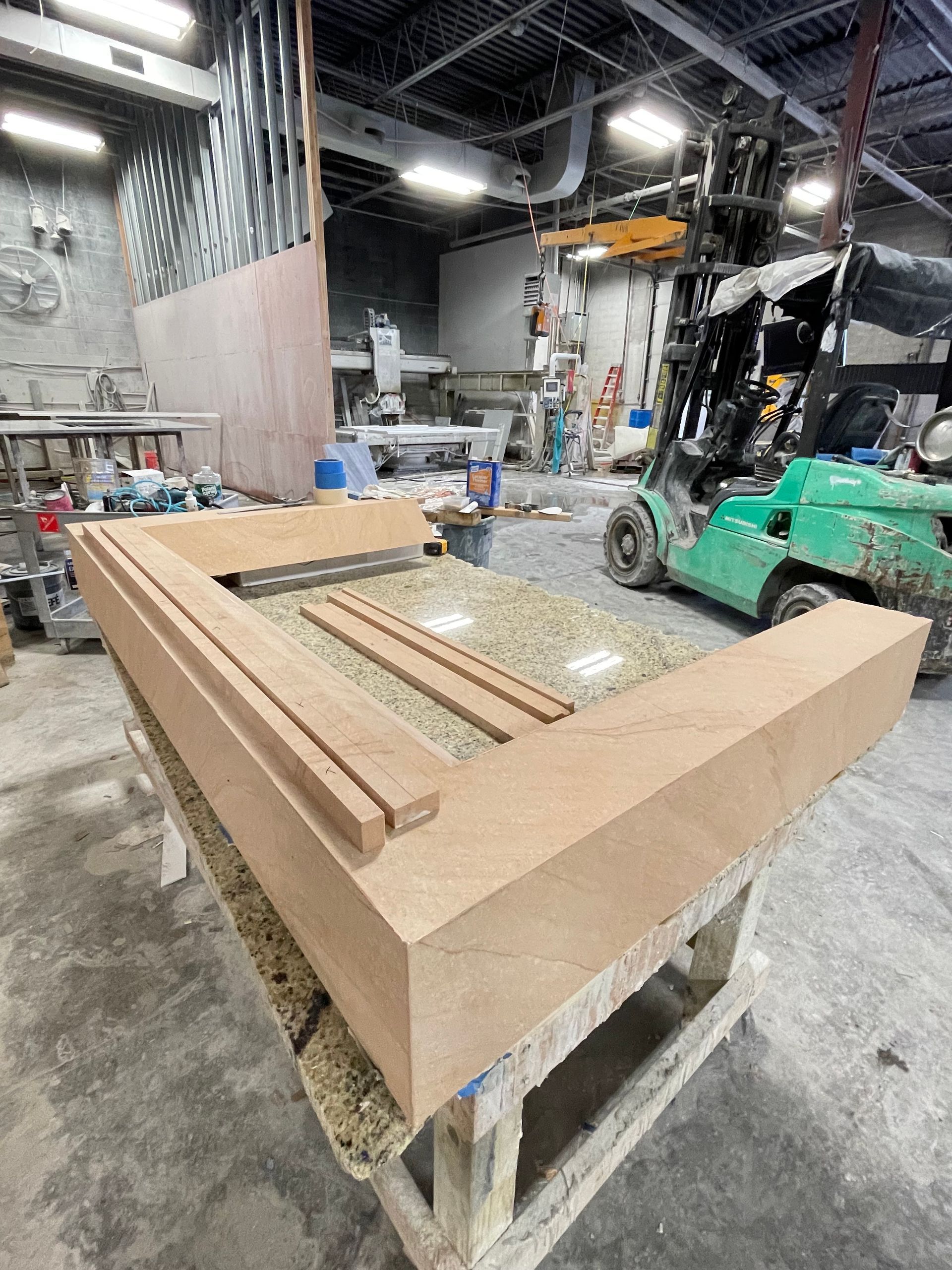 A green forklift is moving a large piece of wood in a factory.