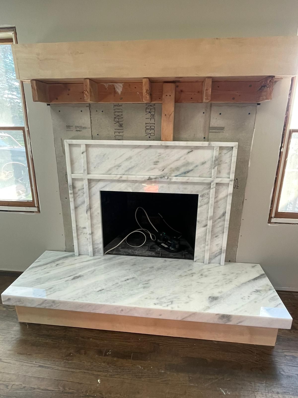 A fireplace with a wooden mantle is being built in a living room.