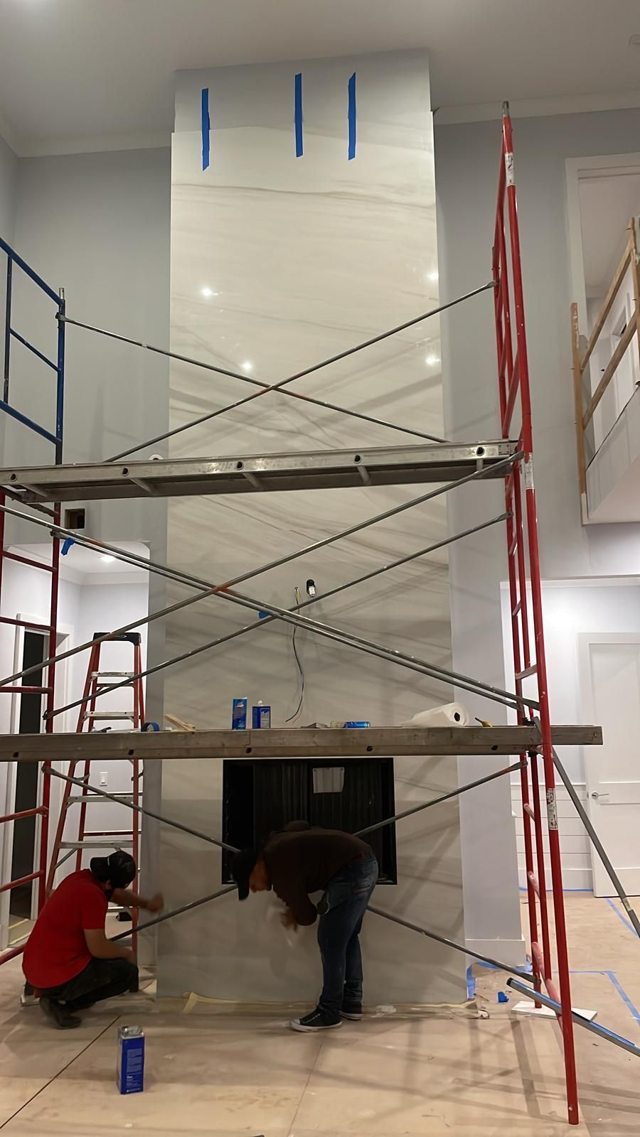 Two men are working on a fireplace in a room with scaffolding.