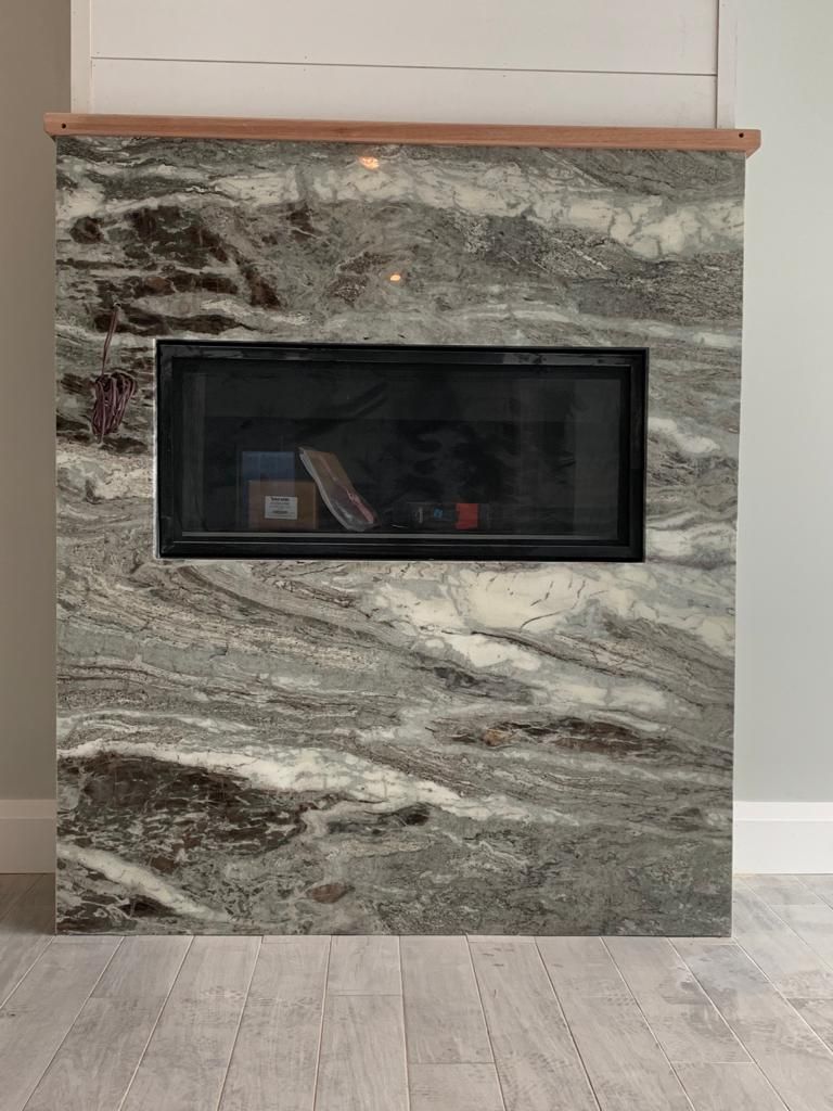 A fireplace with a marble wall and wooden floor in a living room.