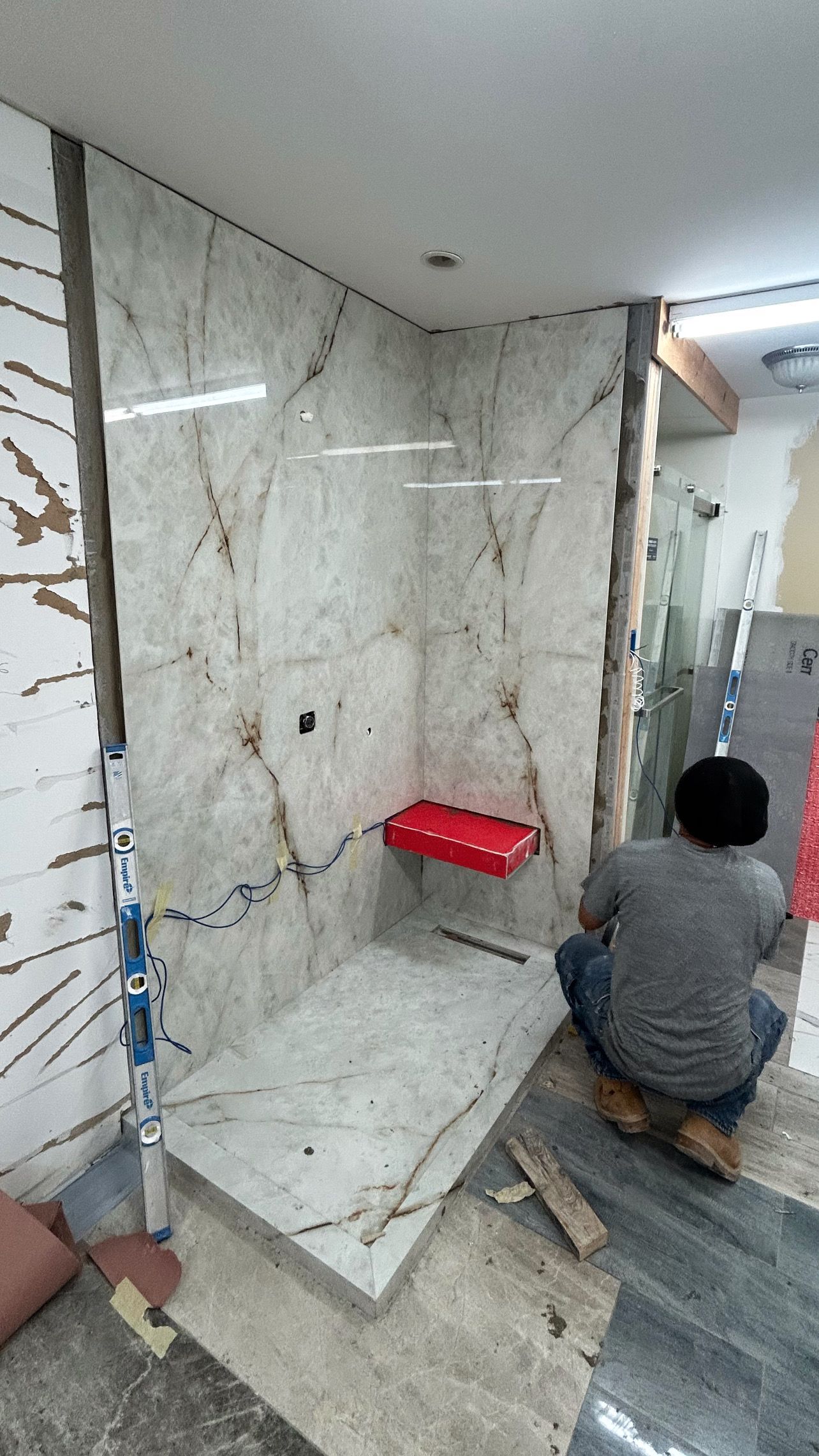 A man is kneeling in front of a shower stall in a bathroom.