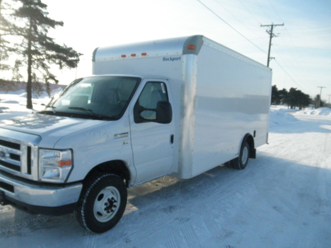 White box truck parked on a snowy roadside beside trees and utility poles