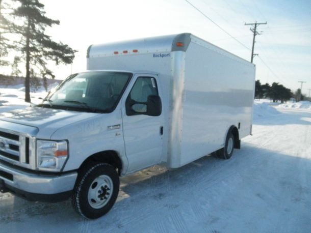 White box truck parked on a snowy roadside beside trees and utility poles