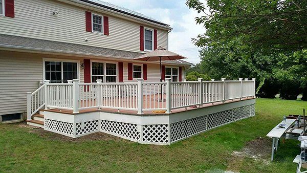 A large deck with a white railing is in the backyard of a house