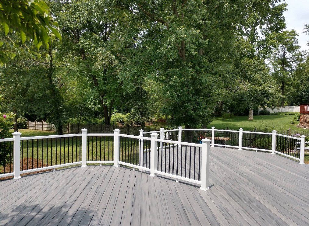 Deck with white posts, black railings, and gray decking; trees in the background.