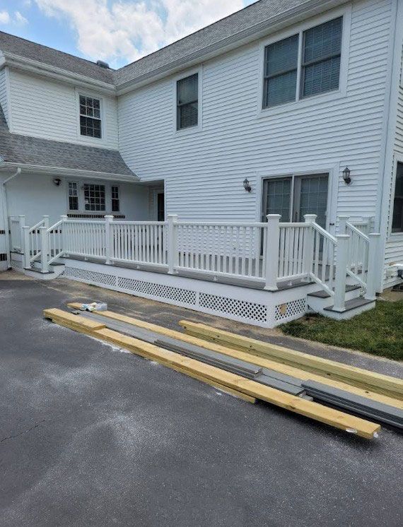 White deck with ramp attached to a two-story white house. Building materials on the blacktop.