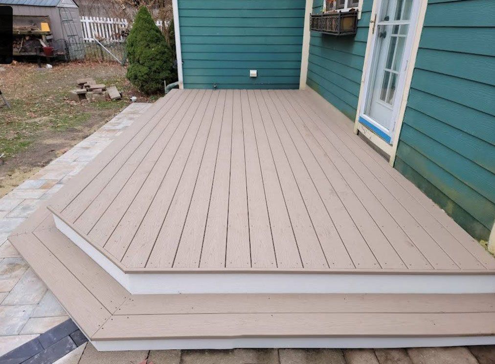 A composite deck with steps, tan boards against a green house exterior, and brick paving.