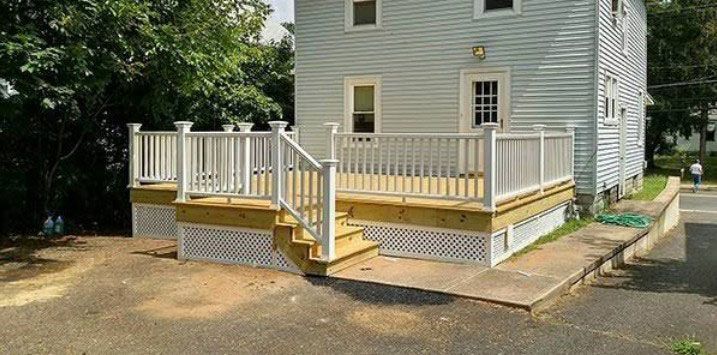 A newly built wooden deck with white railings and lattice skirt, adjacent to a light blue house.