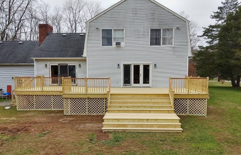 Back of a two-story house with a new wooden deck and stairs; a lawn and trees are in the background.