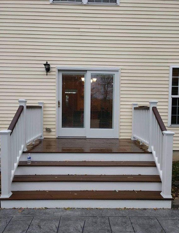 White deck with brown steps leading to a sliding glass door on a house with light yellow siding.