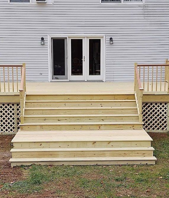 Wooden deck with stairs leading to a house with a sliding glass door. Grass and lattice details.