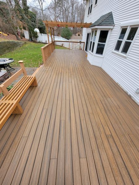 A large wooden deck with a bench and a white house in the background