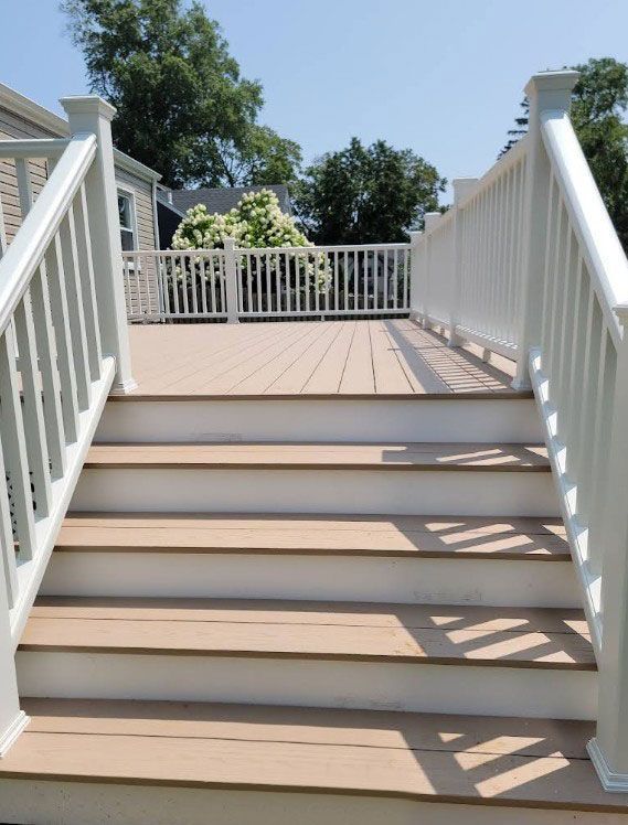 Wooden deck with stairs and white railings, under a clear blue sky.